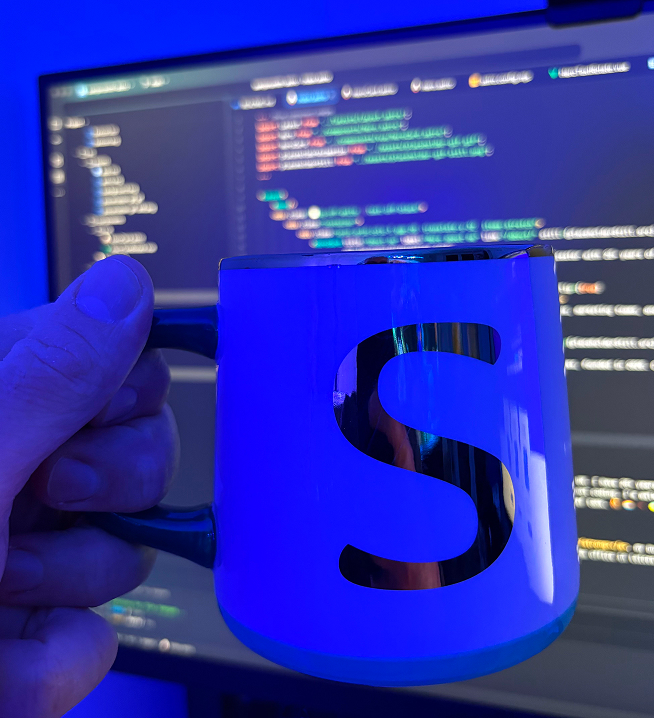 Cup with letter S in front a screen filled with code in the background.